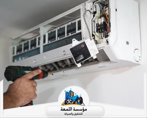 فك وتركيب مكيفات سبليت بالرياض 0502971730 اللمعة فك الأجزاء الإلكترونية لجهاز التكييف، حيث يظهر فني وهو يستخدم مفكاً كهربائياً (Drill) لفك البراغي